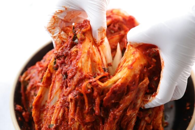 흰 장갑을 낀 손으로 양념을 고루 묻힌 포기김치를 펼친 모습