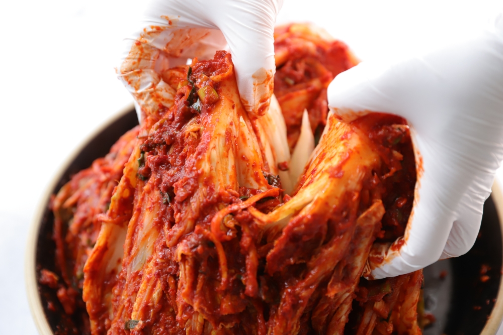 흰 장갑을 낀 손으로 양념을 고루 묻힌 포기김치를 펼친 모습
